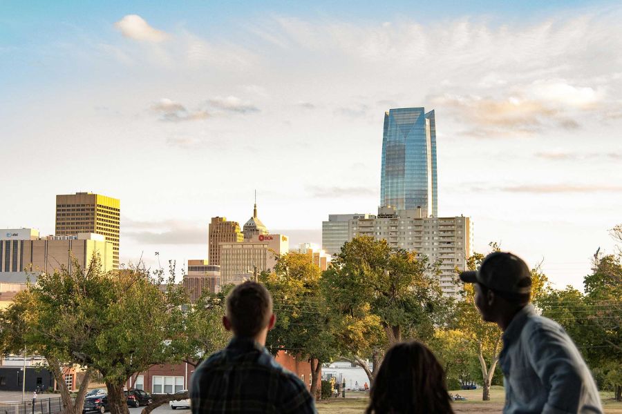 Three people in foreground looking off at the OKC skyline during sunset.