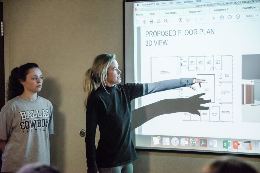 Two students giving a presentation with a plan on the board and one student pointing to the board