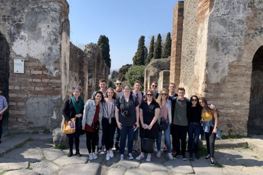A group of students posing between two rustic buildings in Pompei, Italy