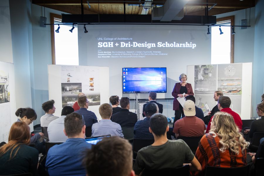 An instructor giving a lecture to a group of 20 people sitting in front of a screen
