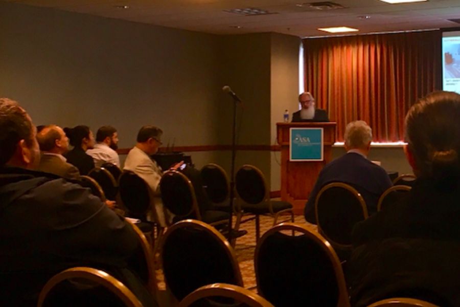 Photo of Daniel Butko presenting at a podium in a dimly lit room