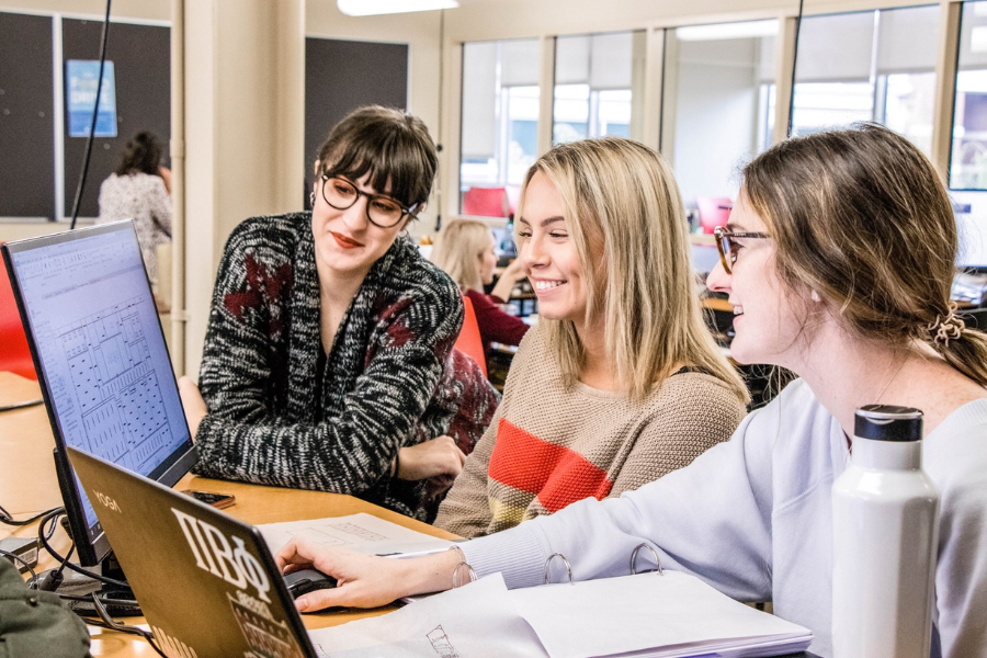 An older mentor assisting two younger students on a computer