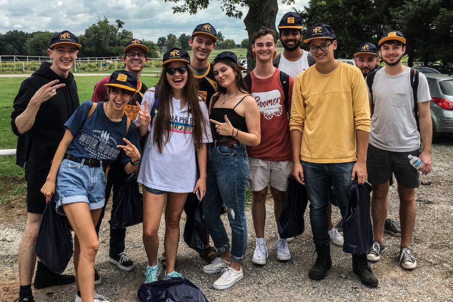 Group of students posing for a picture outside with matching ballcaps