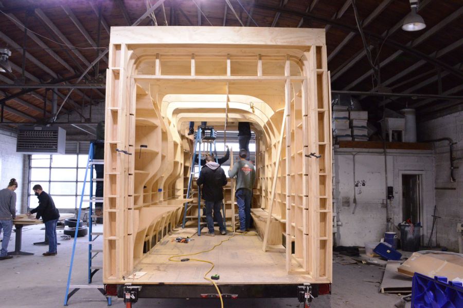 Mobile medical unit inside a workshop under construction with an entirely wood interior with people inside and out of the unit working on construction.  