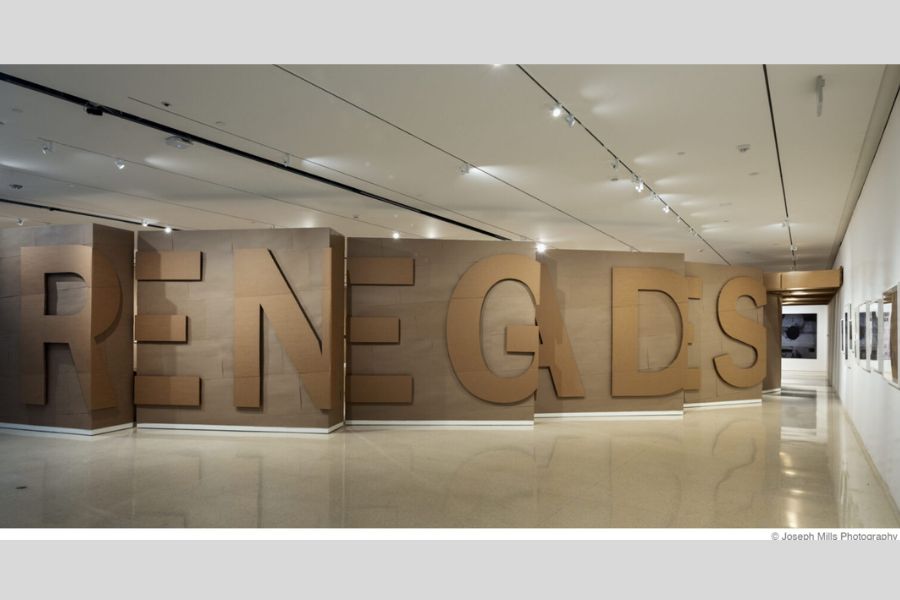 Large-scale exhibition installation spelling “RENEGADES” in oversized cardboard letters arranged across gallery walls inside a museum space.