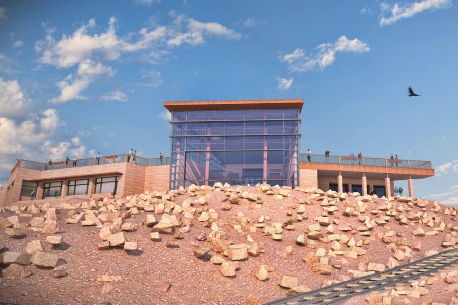 Modern glass visitor center on a rocky mountain summit with a red railway car in the foreground.