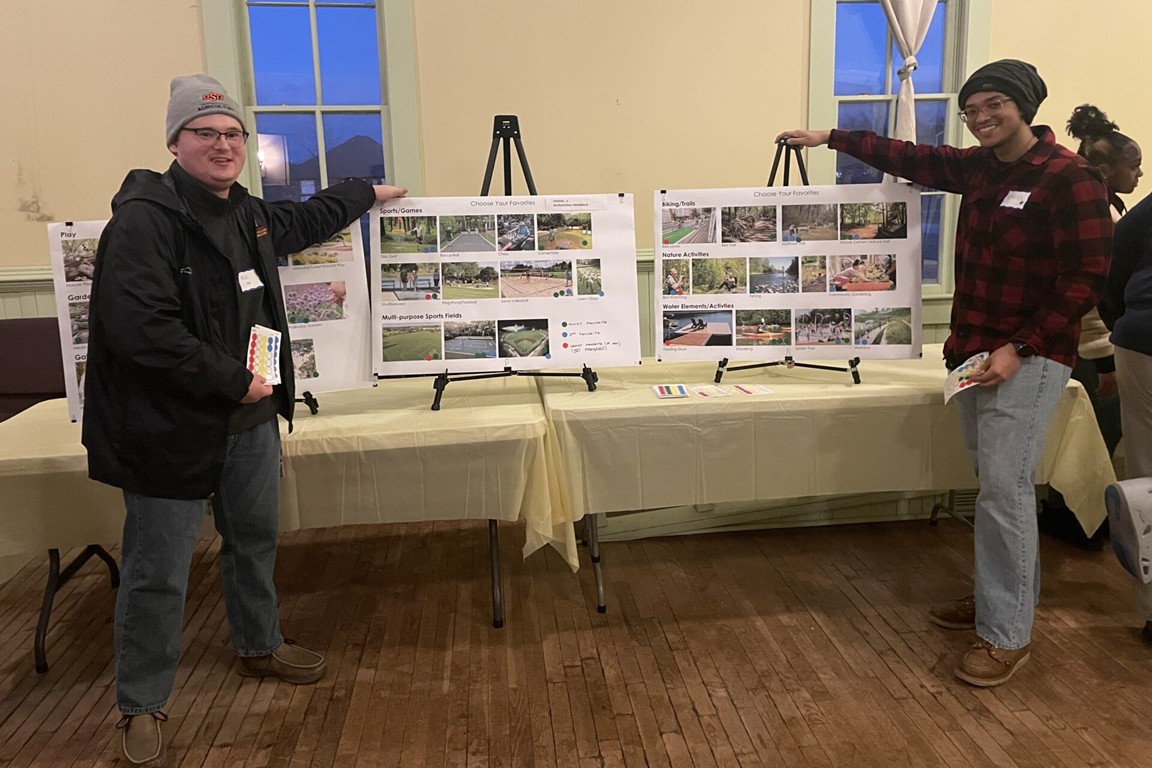 Two students with boards inviting residents to choose their favorite type of park activity.