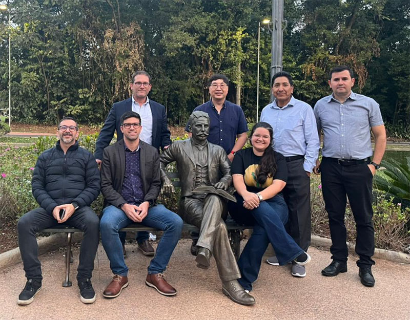 A group of researchers from different groups pose for a photo with a bronze statue.