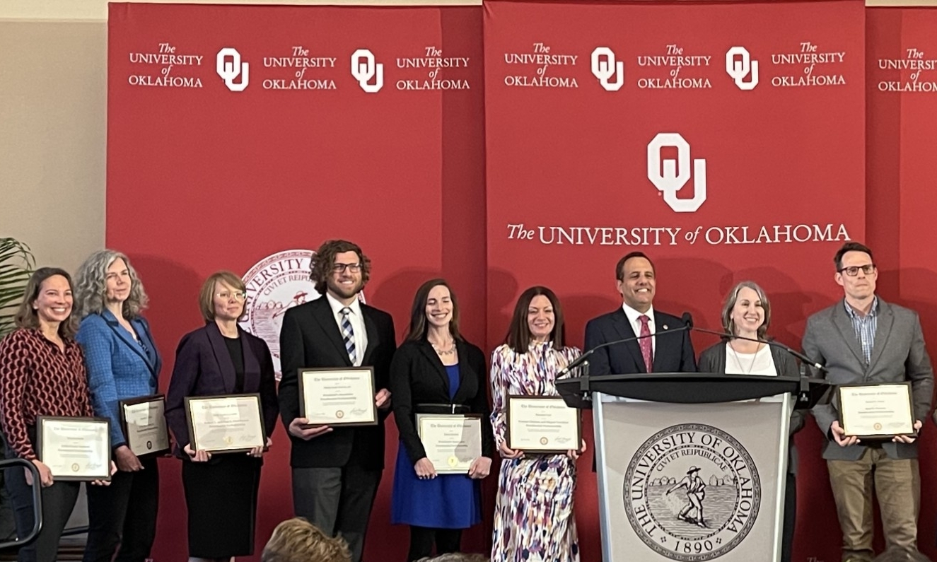 PRofessors standing on stage in front of red OU banner.