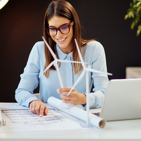 Student looking at energy plans at a desk and holding model of wind turbine