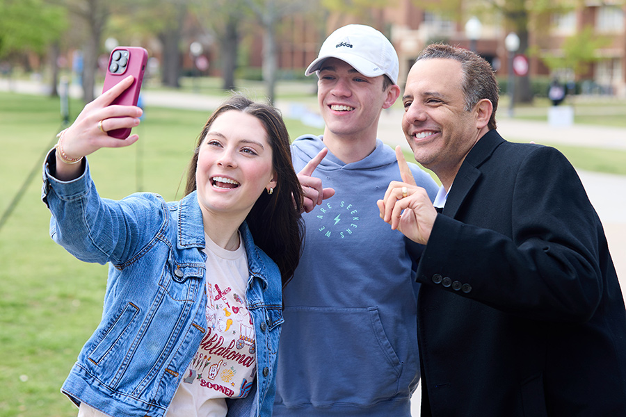 President Joe Harroz taking a selfie with two students on the South Oval of the Norman campus.