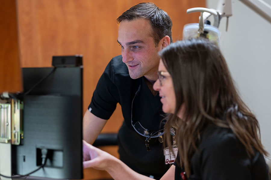 Two people in black scrubs examine a computer screen.