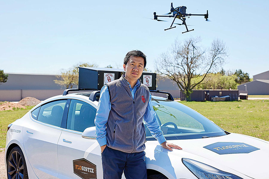 Binbin Wang stands in front of an electric vehicle, a drone flying in the sky above the car.