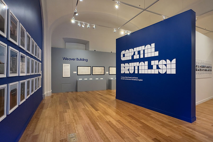 The words "Capital Brutalism" in a blocky white font on a navy blue wall as you enter the Capital Brutalism exhibit.