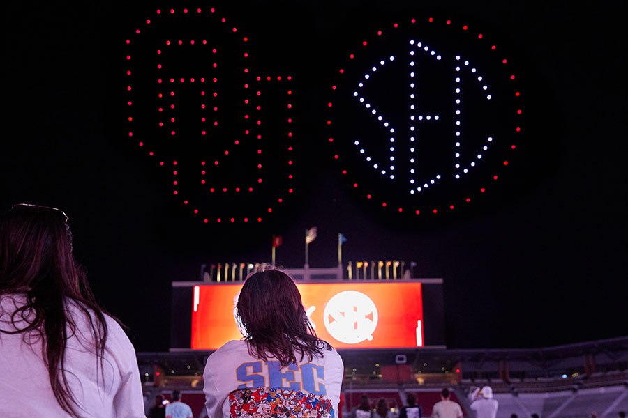 Attendees watch drones show off the OU and SEC logos in the night sky.