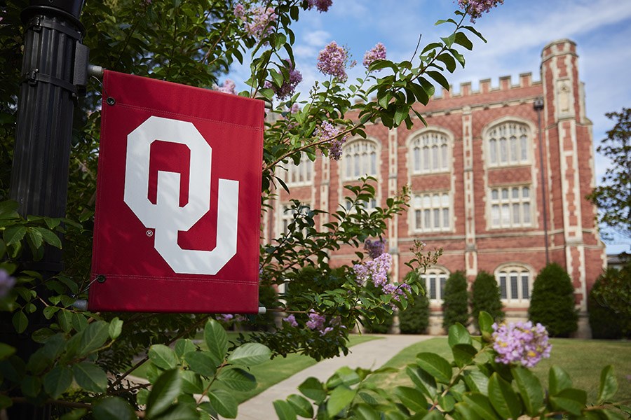 OU flag on University of Oklahoma campus in front of campus building.