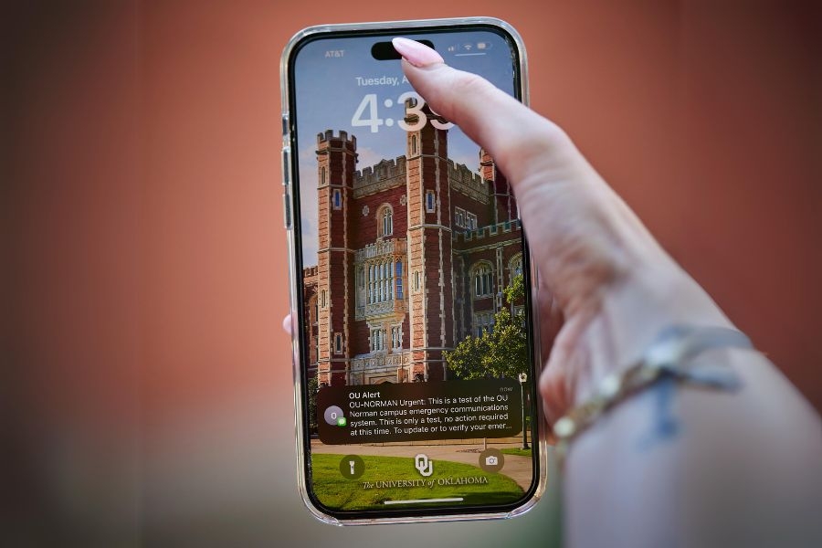 A hand holding a cell phone showing an OU-Alert text.