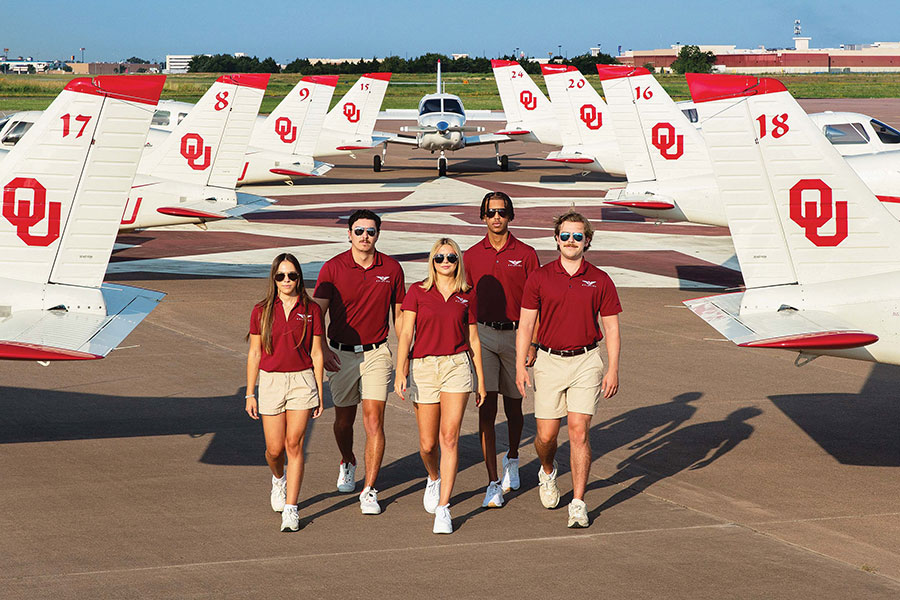 Five School of Aviation students walking through an aisle created by planes.