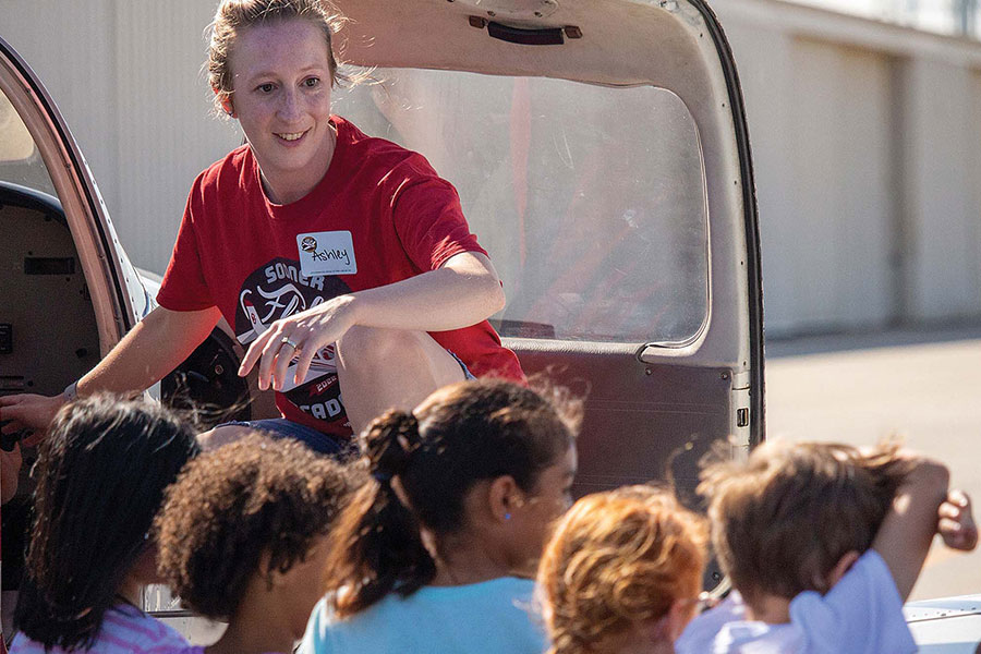 Ashley Crisman stands on a plane wing looking over the heads over children.