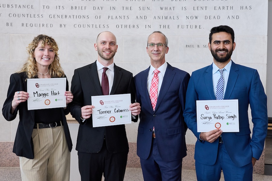 Four people stand in a line, with the three students holding up certificates.