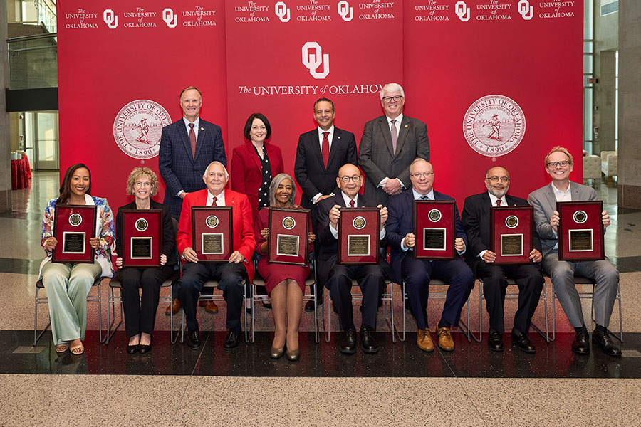 Eight people sitting in chairs holdings awards, with four people standing behind them.