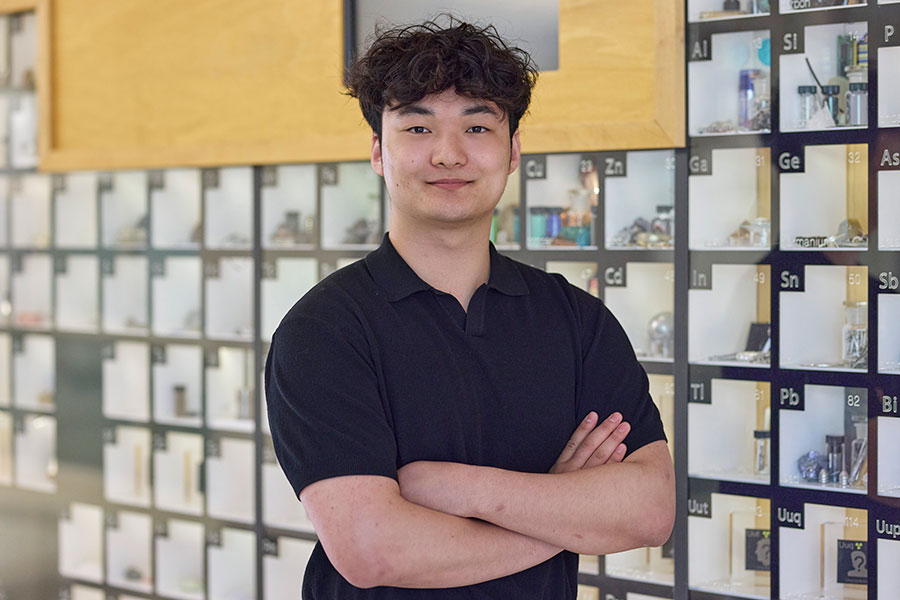 Man standing in front of large periodic table containing elemental samples.