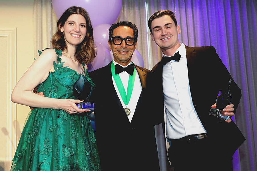 Photograph of three people at an awards ceremony, with two holding trophies and one wearing a medal.