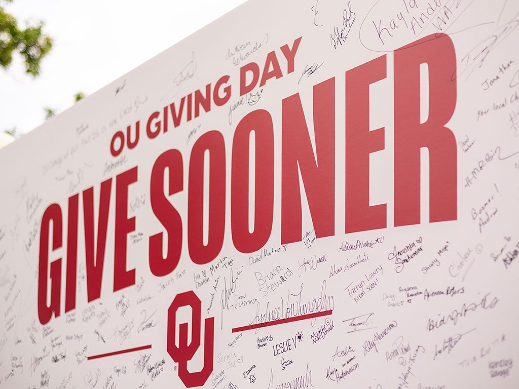 A sign that reads "OU Giving Day Give Sooner" with the OU interlock below. The sign is covered with signatures.