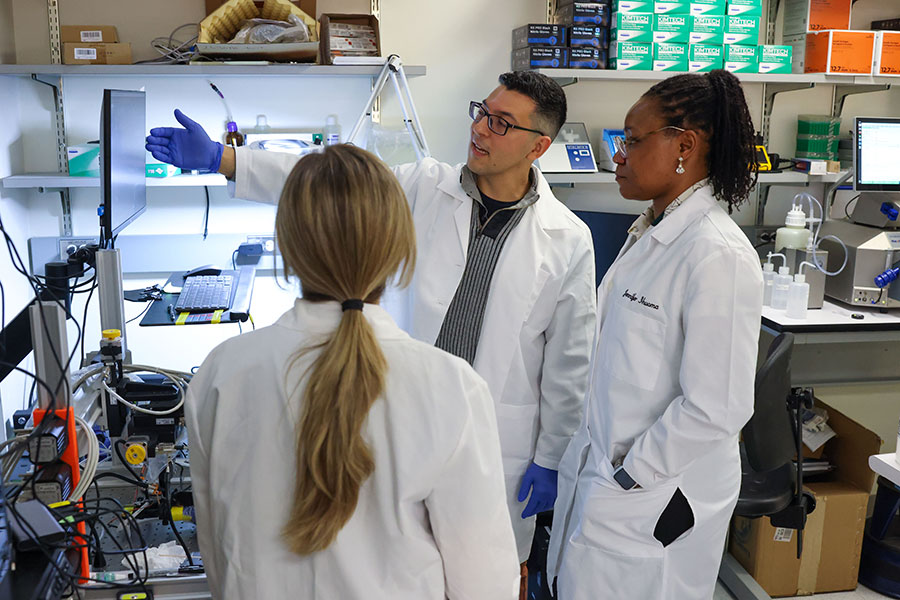 Three doctors in white coats stand in a lab looking at a screen.