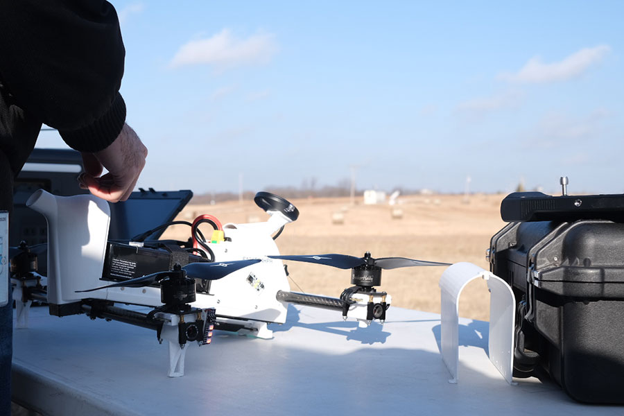 A drone sits on a table on a field while a researcher stands next to it.