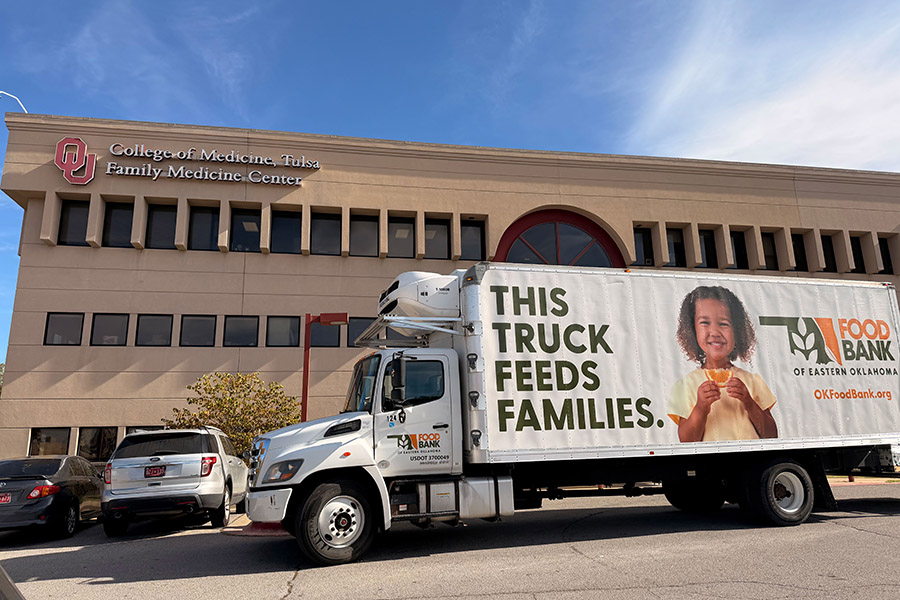 A large truck with a wrap that reads "This Truck Feeds Families," parked outside of the University of Oklahoma Family Medicine building.