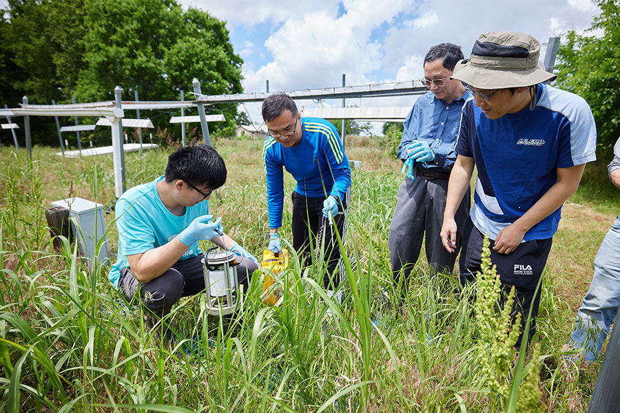 A group of scientists stand in a field of grass holding equipment.