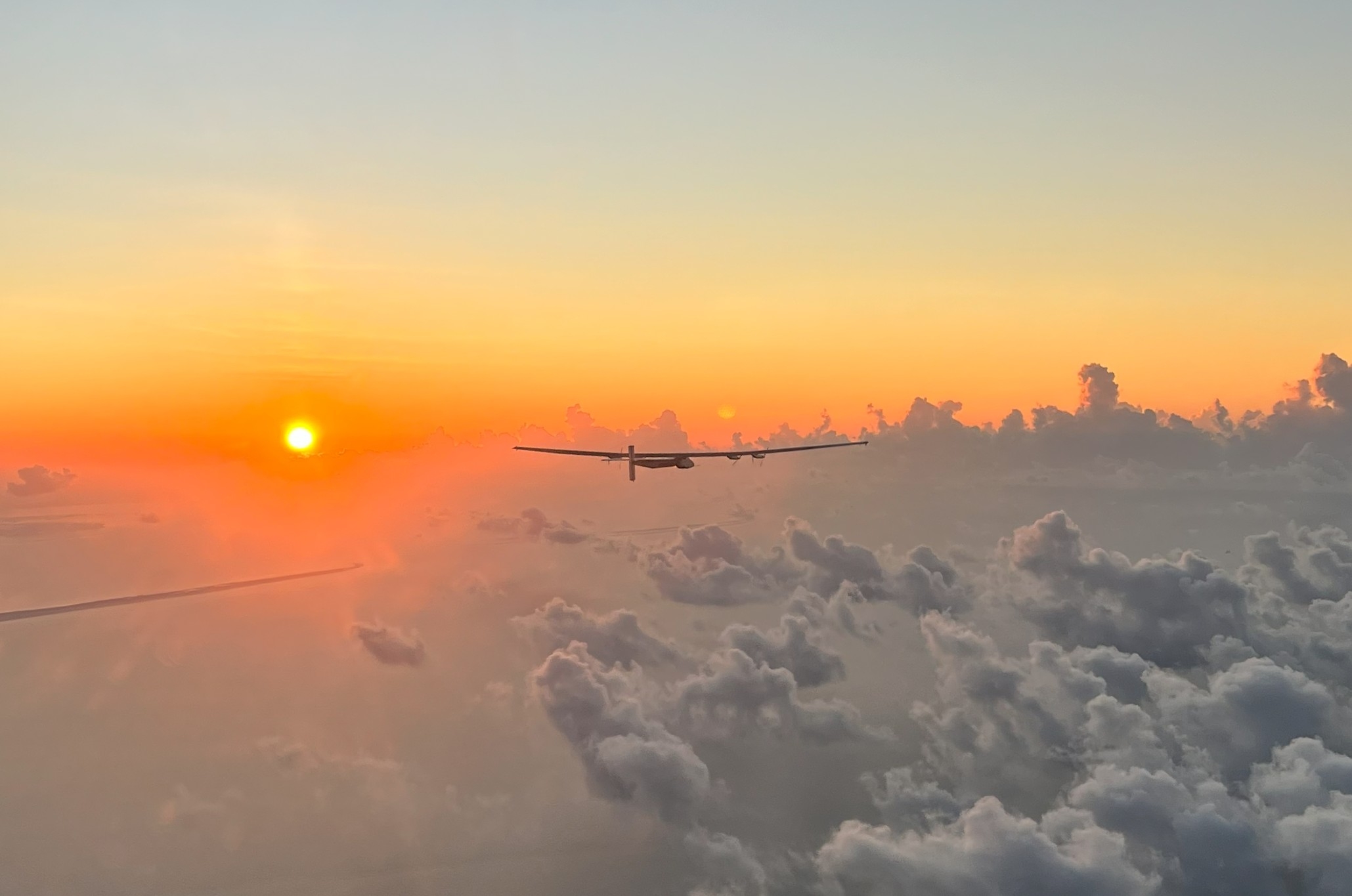 A plane-size drone flying toward a sunset.