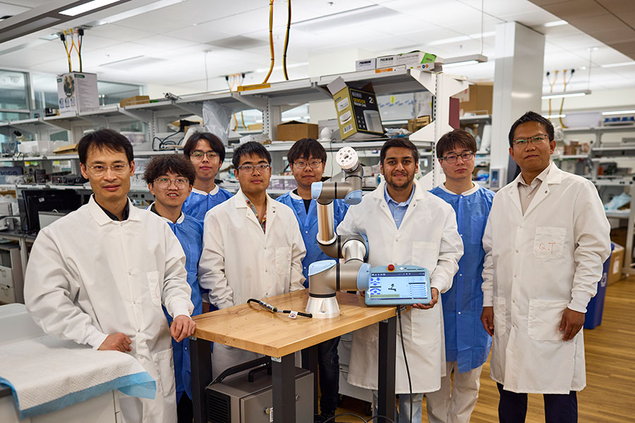 A group of researchers in lab coats surround a table in a lab showcasing a device.
