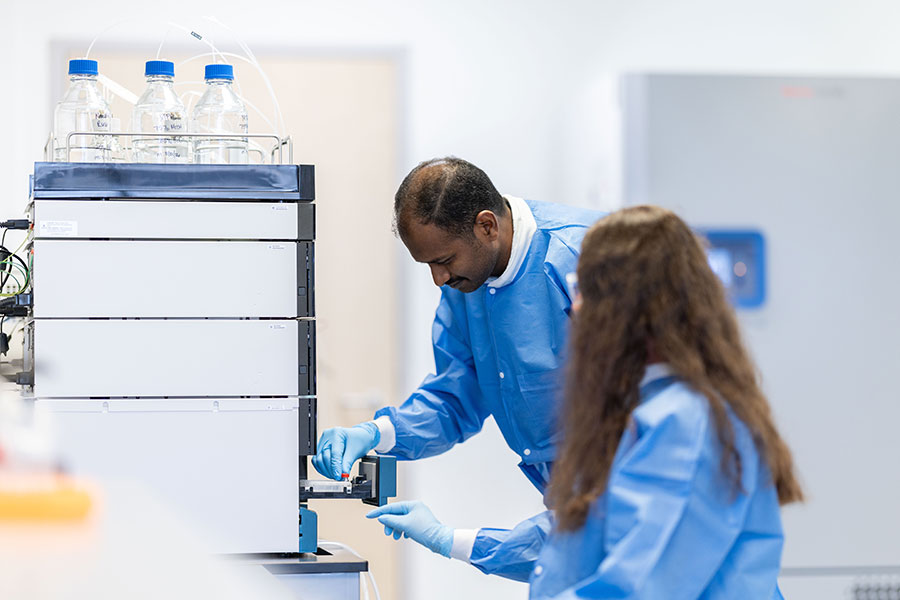 Two individuals in blue lab coats operate a device in a labratory.