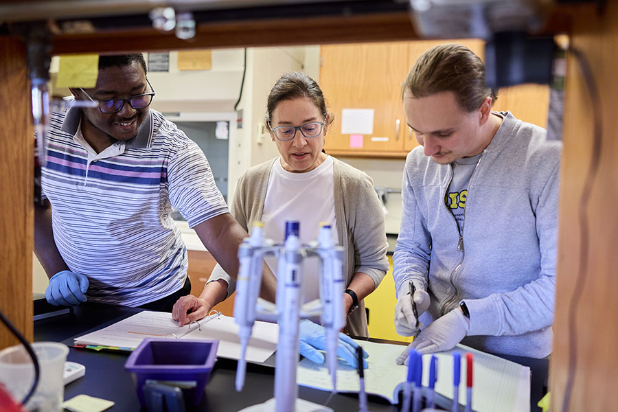 Three researchers examine a paper while in a laboratory.