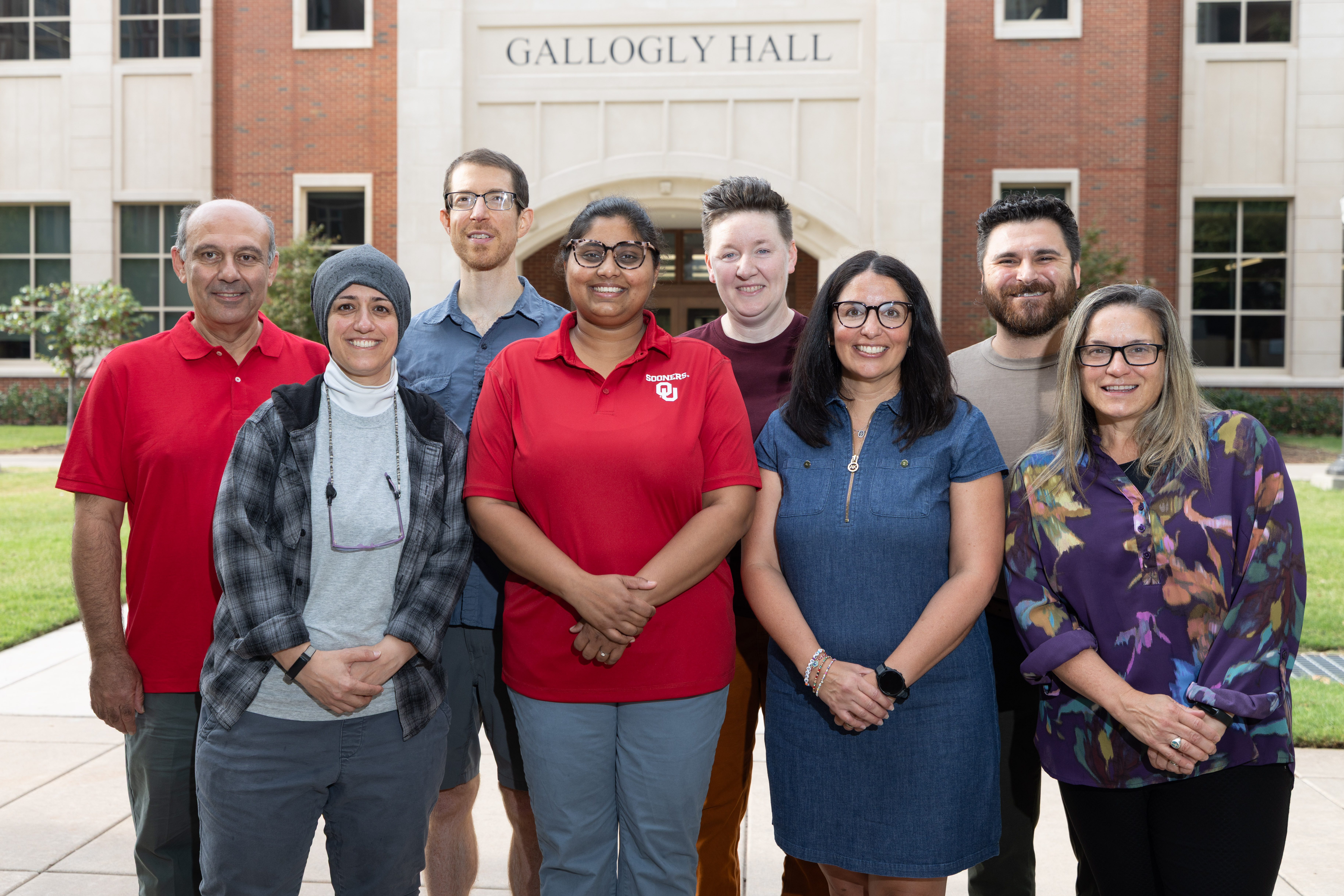 A group of adults stand together and smile in front of a building labeled Gallogly Hall.