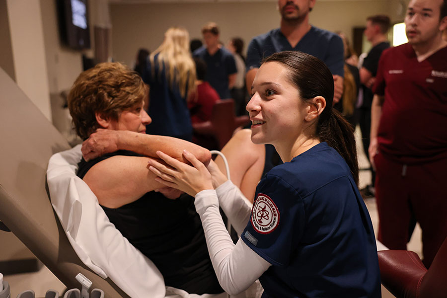 A woman in a dark blue lab coat holds a female patient's arm in a lab setting.