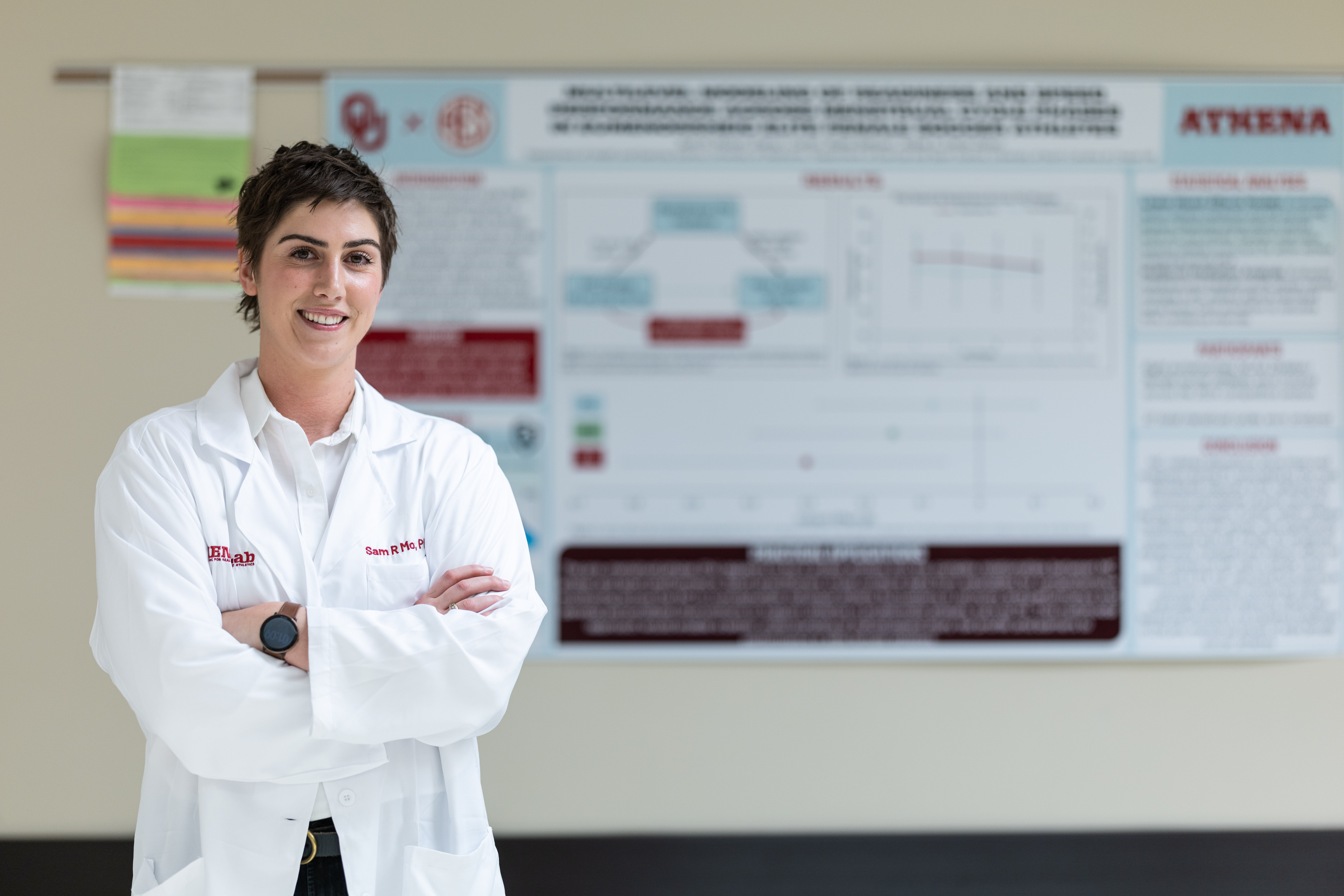 A woman in a lab coat stands in front of a research poster.