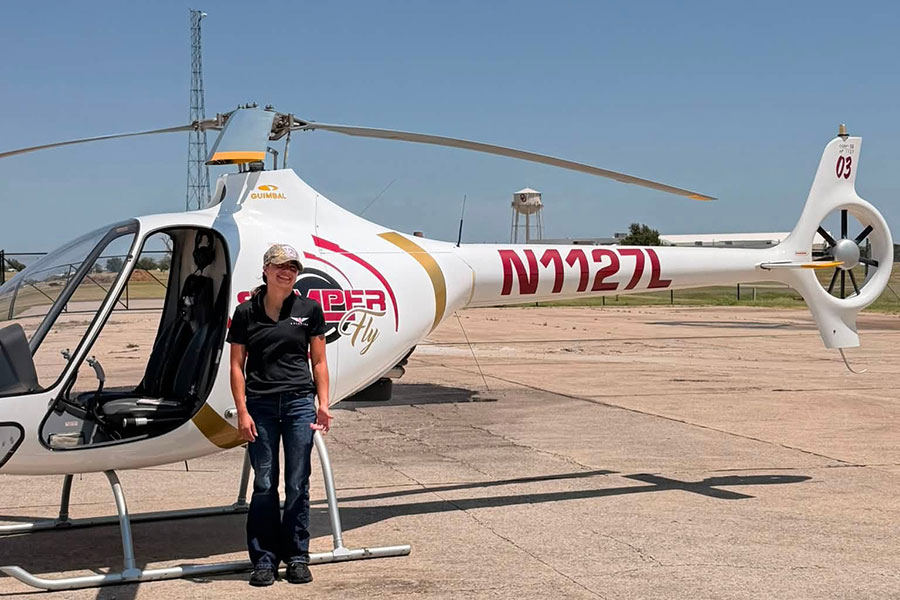 Naomi Ellis stands next to a Semper Fly helicopter at an airfield.