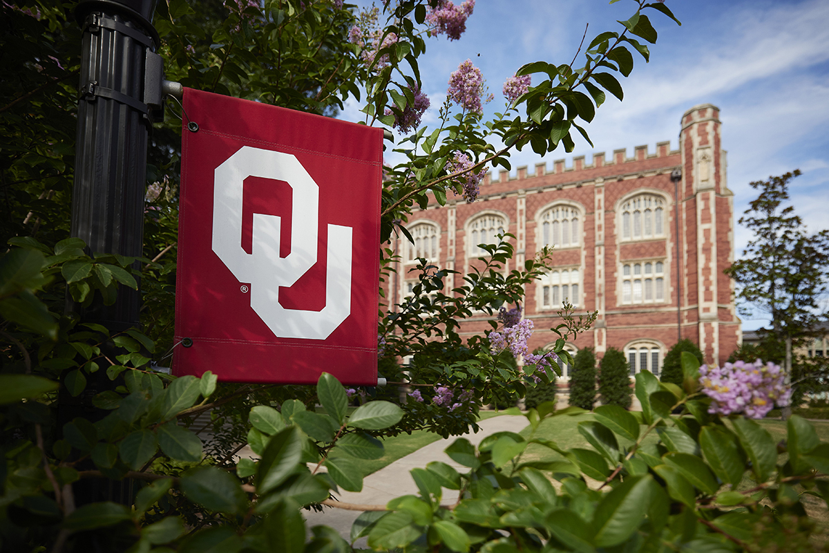 OU flag on University of Oklahoma campus in front of campus building.