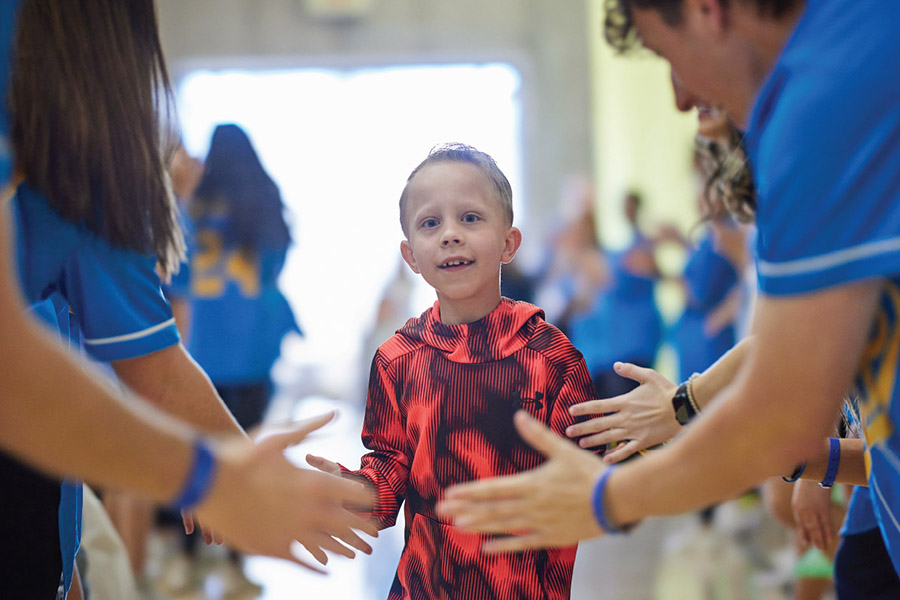 Young child walks through a welcome line of OU students getting high fives as he enters 2024 Dance Marathon event.