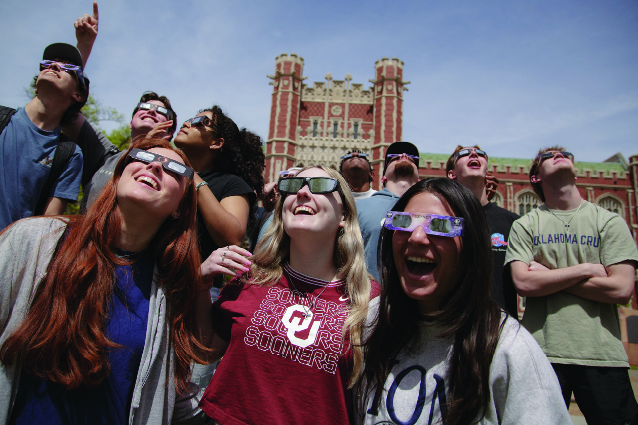 Large group of students gather in front of the Bizzell library with their solar glassed to view the eclipse