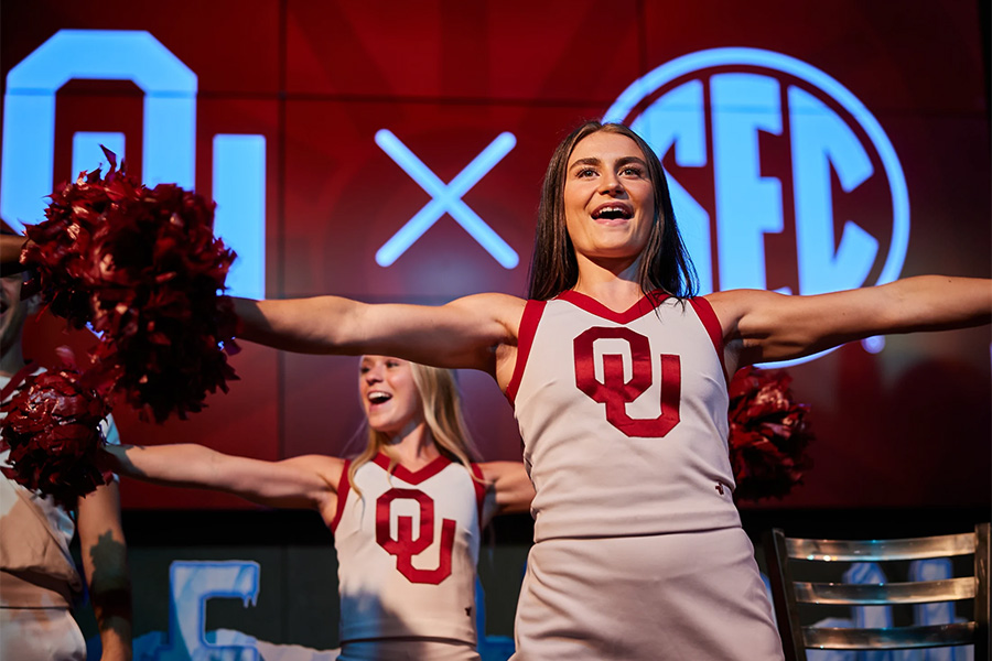 OU Cheerleaders perform in stage in front of a screen that reads OU x SEC.
