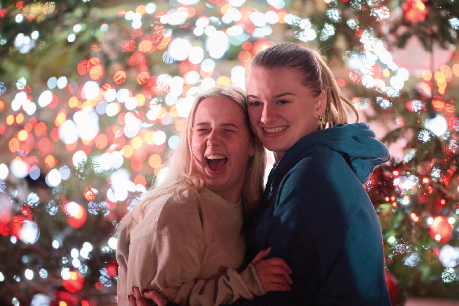 Two students pose for a photo in front of brilliant red and white holiday lights.