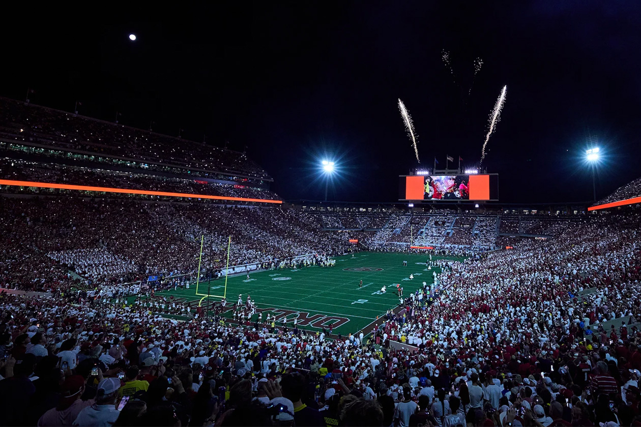 A packed Gaylord Family Oklahoma Memorial Stadium at night, with fireworks in the background.