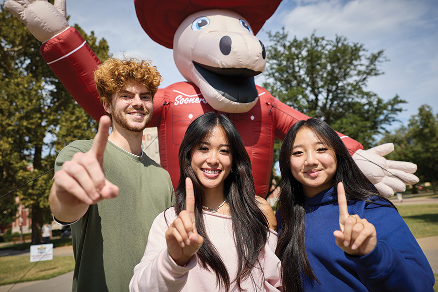 Three students holding up their index finger in front of an inflatable mascot.