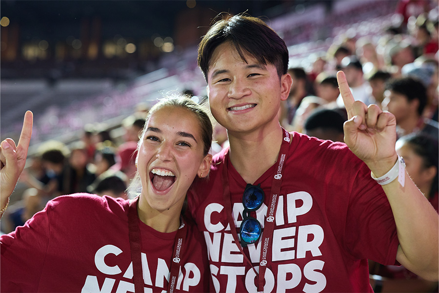 A female student and a male student holding up the O-U hand sign and wearing "Camp Never Stops" crimson shirts.