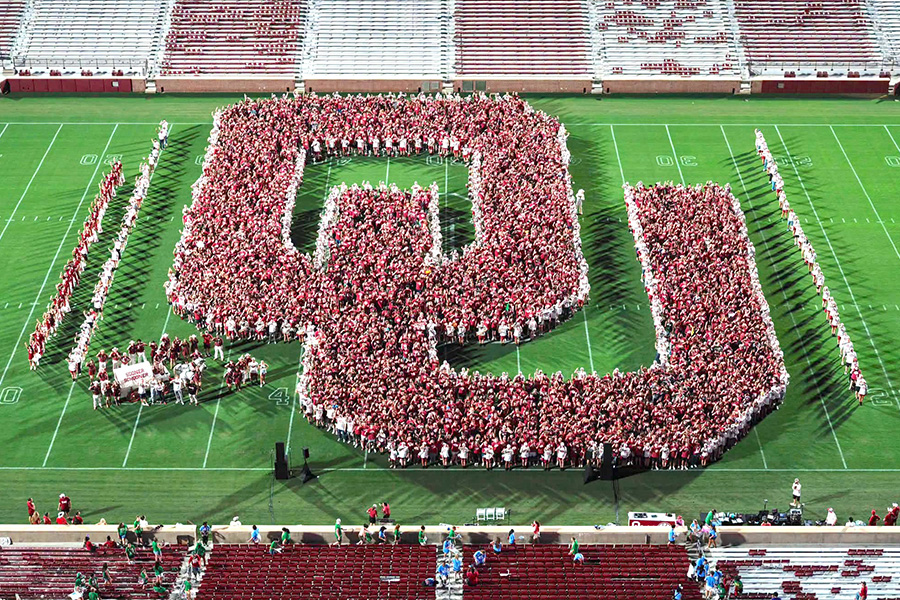 The O-U logo made from the newest class of freshmen standing together in red and white shirts on the football field.