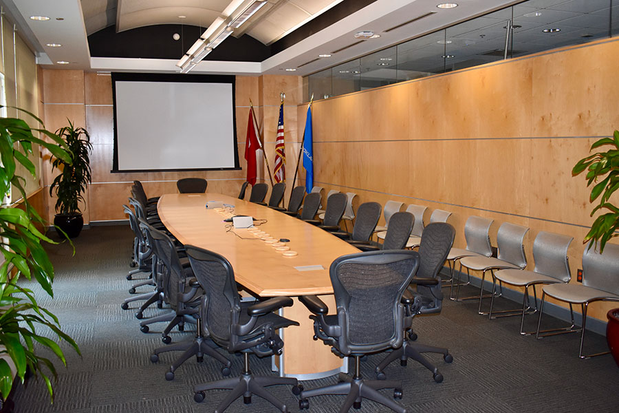 The National Weather Center Boardroom, with a large table an chairs in the middle and flags and a projection screen in the back.